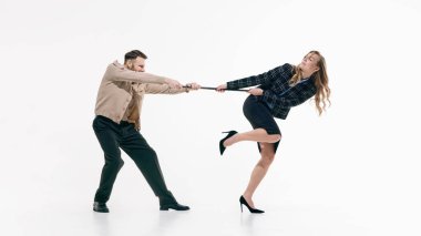 İş adamı ve iş kadını, dinamik stüdyoda objeleri zıt yönlere çekiyorlar. Beyaz arka planda poz veriyorlar. Kurumsal rekabet, ortaklık gerilimi, takım çalışması anlaşmazlığı ve müzakere kavramı