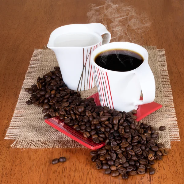 Kahve fincan tabağı, süt kabı ve masada kahve çekirdekleri ile