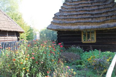 Tahta çitlerle çevrili bir açık hava müzesinde eski bir ahşap ev ve bir sürü çiçek ve bitki.