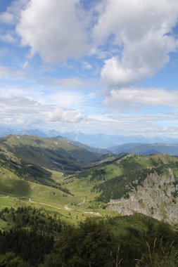 Dağların ve vadilerin manzarası, yeşil, bitki örtüsü ve tepeler arasındaki yol, mavi gökyüzü ve bulutlar