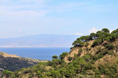 Dağların manzarası, ağaçlarla, çamlarla kaplı tepeler, arka planda deniz ve kıtasal İtalya manzarası.