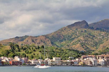 mountain view over the sea, above them a lot of dense white clouds, mountains descending into the sea, boats at sea, Sicily, a bay with moored barges and boats