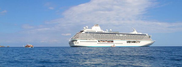 big seagoing passenger ship in the sea and next to it a small boat, blue sea and blue sky