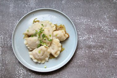 yuvarlak tabak, kızarmış soğan yastığında buharda pişirilmiş hamur tatlısı, tabakta karbonhidrat, hamur köftesi, yeşil soğan serpiştirilmiş sıcak köfte, sıcak yemeğin üstünde buhar.