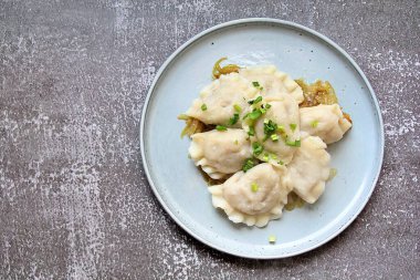 yuvarlak tabak, kızarmış soğan yastığında buharda pişirilmiş hamur tatlısı, tabakta karbonhidrat, hamur köftesi, yeşil soğan serpiştirilmiş sıcak köfte, sıcak yemeğin üstünde buhar.