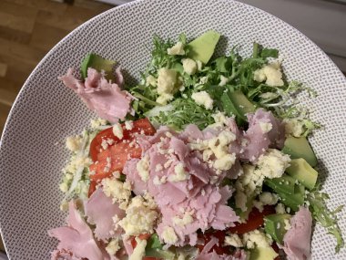 Avokado salatası, jambon, marul ve kırmızı biber, üzerine ezilmiş peynir ve taze salata serpiştirilmiş.