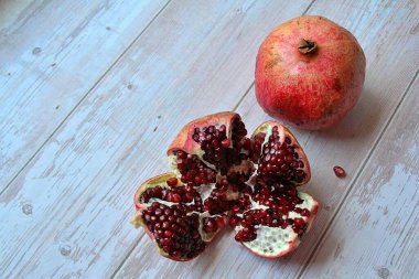 İki nar, kırmızı meyve, hafif ahşap zemin üzerinde nar, açık nar ve sulu kırmızı nar tohumu.