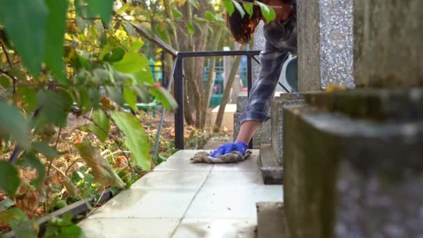 Cleaning cemetery. A woman washes grey paving slabs and monument grave with rag. — Stock Video