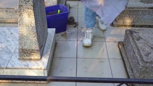 Cementerio de limpieza. Una mujer lava losas de pavimentación gris y tumba monumento con trapo. — Vídeo de stock