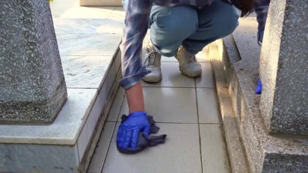 Membersihkan kuburan. Seorang wanita mencuci monumen abu-abu di kuburan dengan kain. — Stok Video