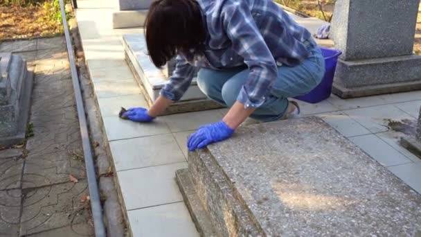 Cleaning cemetery. A woman washes grey paving slabs and monument grave with rag. — Stock Footage Cleaning cemetery. A woman washes grey paving slabs and monument grave with rag. Video Clip