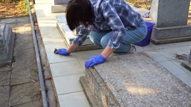 Cleaning cemetery. A woman washes grey paving slabs and monument grave with rag. — Stock Video