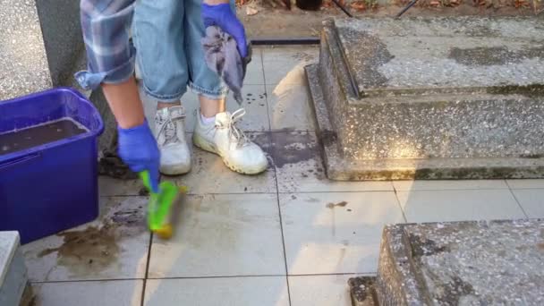 Il cimitero delle pulizie. Una donna lava lastre grigie pavimentazione e tomba monumento con straccio. — Video Stock