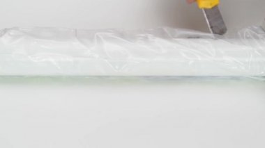 Eller masanın bacağındaki plastik ambalajı kesmek için kırtasiye bıçağı kullanır..