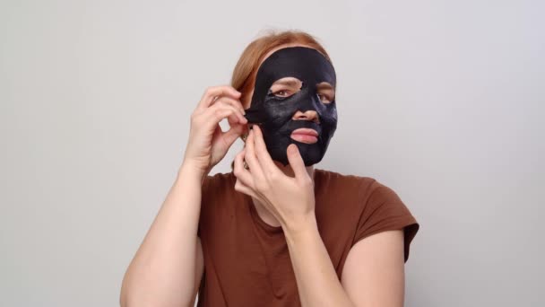 Kobieta wygładza czarną maskę kosmetyczną na twarzy. — Wideo stockowe