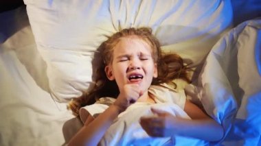 Üstü görünüyor. Küçük kız hasta, yatakta yatıyor ve öksürüyor.. 