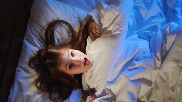 Blick von oben. Ein Mädchen liegt verängstigt im Bett und deckt das Gesicht mit einer Decke zu. — Stockvideo