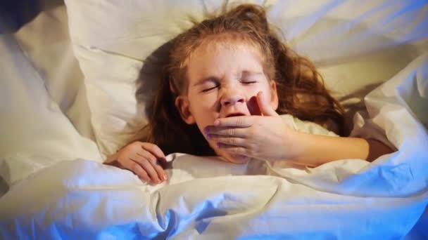 Vista desde arriba. Una niña somnolienta yace en la cama y bosteza. — Vídeos de Stock