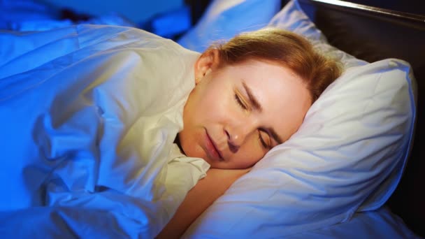 Een vrouw met rood haar slaapt op haar zij in bed en ziet stille dromen, glimlacht. — Stockvideo