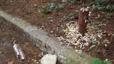 Paslı sütunun yanında bir sürü sigara izmariti ve enkaz var.