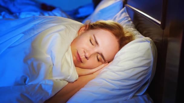 Žena s rudými vlasy spí na boku v posteli a vidí tiché sny. — Stock video