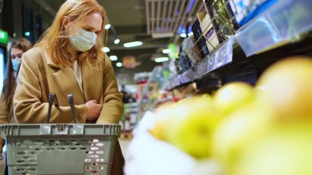 Eine Frau in einer schützenden Einwegmaske beim Einkaufen im Supermarkt — Stockvideo