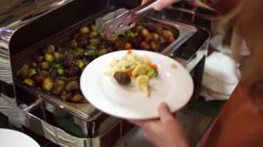 Kahvaltı, otelde büfe. İnsanlar tabaklarına yemek koyar.