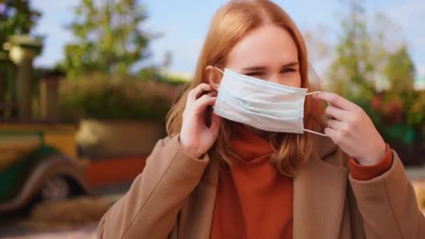 Eine Frau im Mantel trägt im Stehen eine medizinische Einmalmaske — Stockvideo