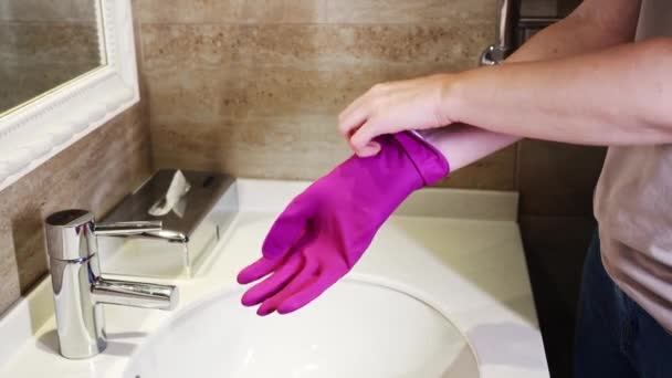 Before cleaning the bathroom, woman puts on her hands rubber protective gloves — Stock Video