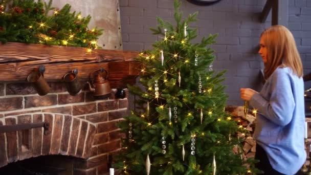 A woman dresses up Christmas tree in a country house near the fireplace — Stock Video