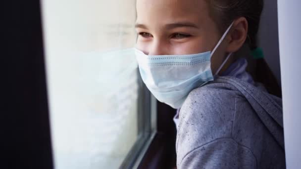 Boldog tini lány védő maszkban, nézz ki az ablakon. — Stock videók
