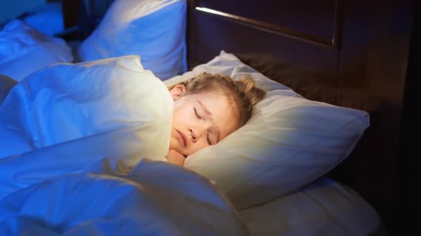 Una bambina dorme a letto, vede un incubo e copre il viso con una coperta. — Video Stock