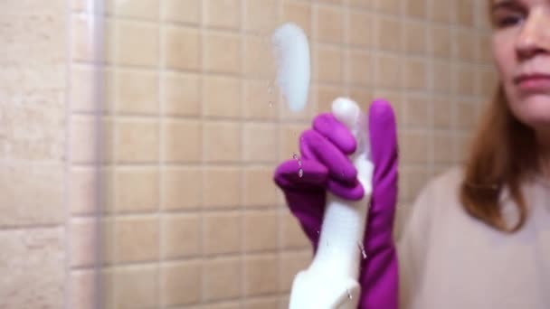 Frau in Handschuhen, mit Waschmittelspray, Lappen wäscht Trennwand in der Dusche — Stockvideo