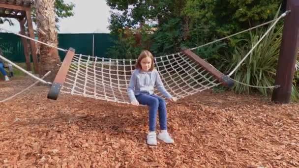 Ein Teenager-Mädchen schaukelt auf einer Hängematte auf einem Kinderspielplatz im Park. — Stockvideo