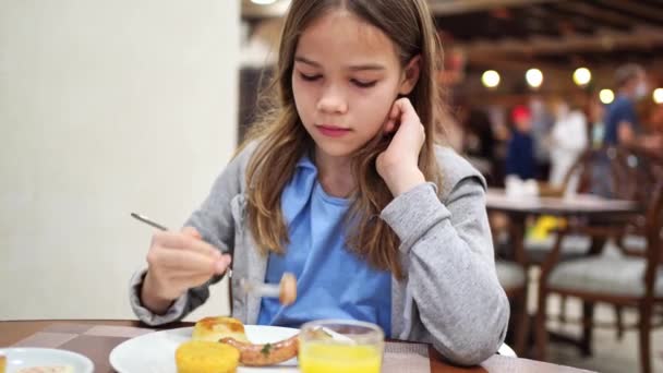 Een meisje eet een worst en drinkt sap in de eetkamer.. — Stockvideo