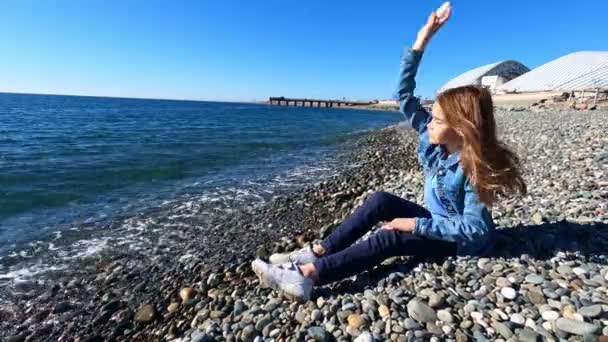 Flicka kastar stenar i vatten och skämt när du sitter på stranden. — Stockvideo