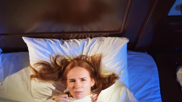Vista superior. una mujer yace en la cama bajo una manta blanca y asustada, asustada. — Vídeo de stock