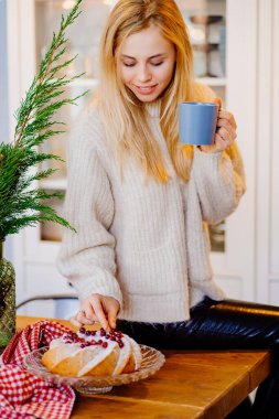 a young woman drinks hot cocoa sitting on the kitchen table. Christmas pastries.