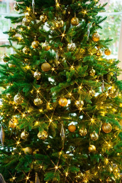 Árbol de Navidad artificial decorado con juguetes de oro y bulbos de guirnalda. —  Fotos de Stock