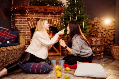 woman having fun and eating tangerines by fireplace with New Years decoration