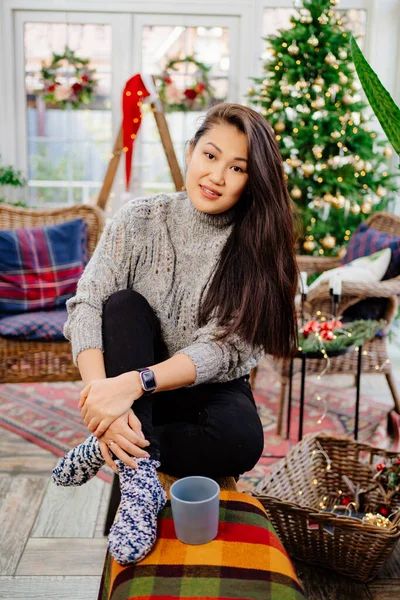 A beautiful brunette woman sits in a country house decorated for the new year