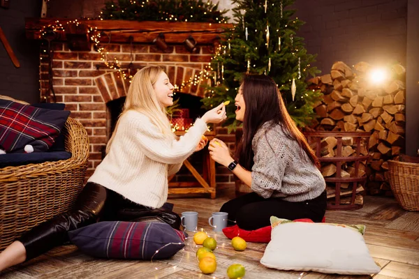 woman having fun and eating tangerines by fireplace with New Years decoration