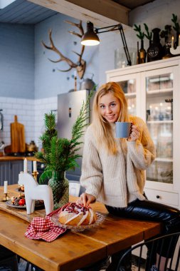 a young woman drinks hot cocoa sitting on the kitchen table. Christmas pastries.