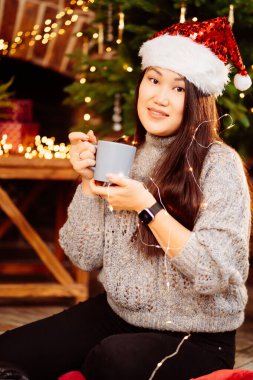 A beautiful woman sits on floor near fireplace in house decorated for new year. 