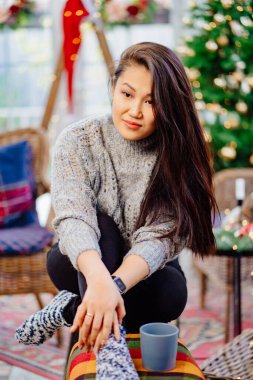 A beautiful brunette woman sits in a country house decorated for the new year