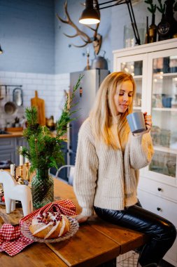 a young woman drinks hot cocoa sitting on the kitchen table. Christmas pastries.