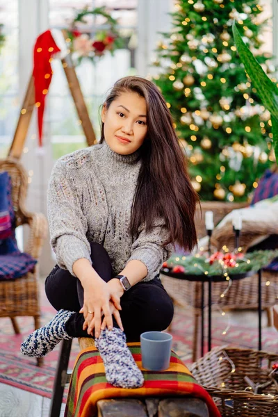 A beautiful brunette woman sits in a country house decorated for the new year