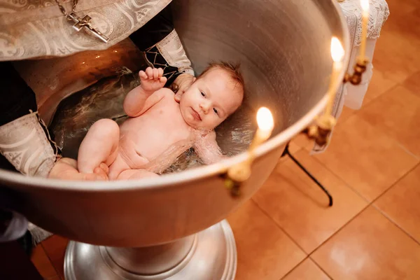 Ein Kind wird bei einer christlichen Taufe in der Kirche in einem Brunnen ins Wasser gelassen — Stockfoto