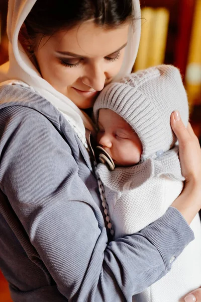 Красива мама в хустці з маленькою дитиною на руках у церкві . — стокове фото
