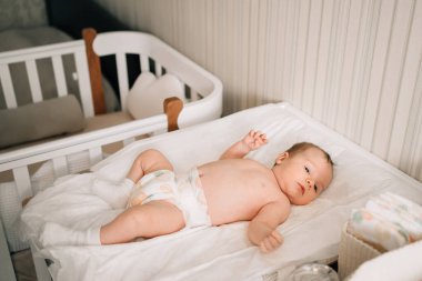 A baby on a white sheet on the changing table in the nursery. 